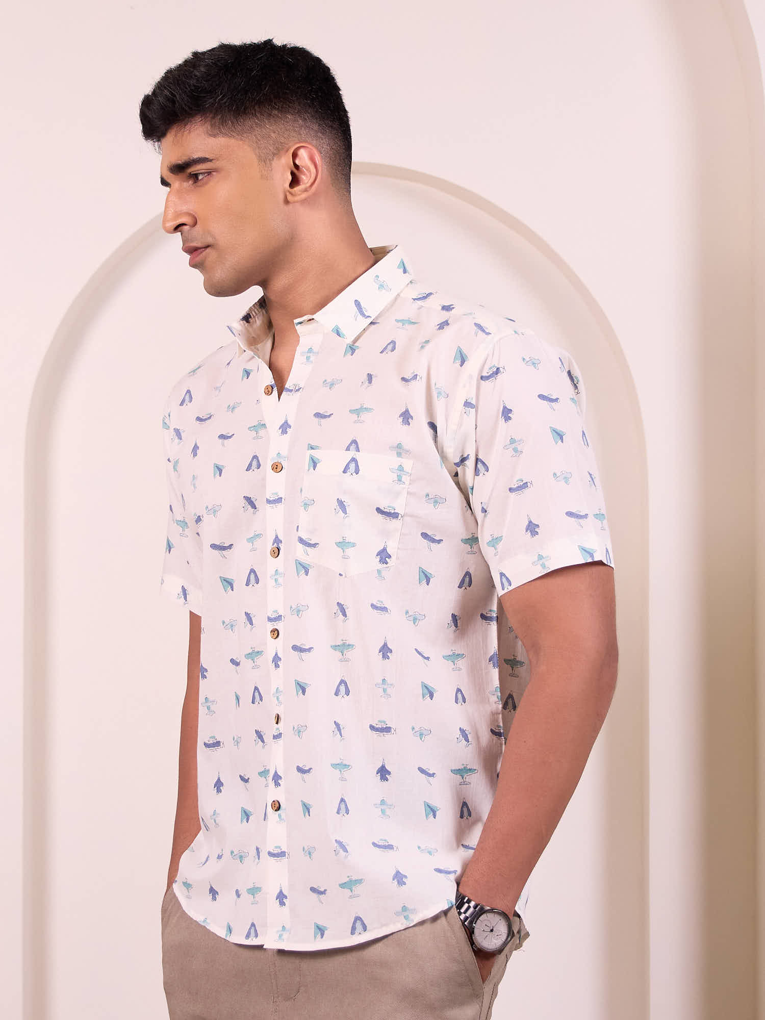 Man wearing a white short-sleeve shirt with blue patterns against a beige background