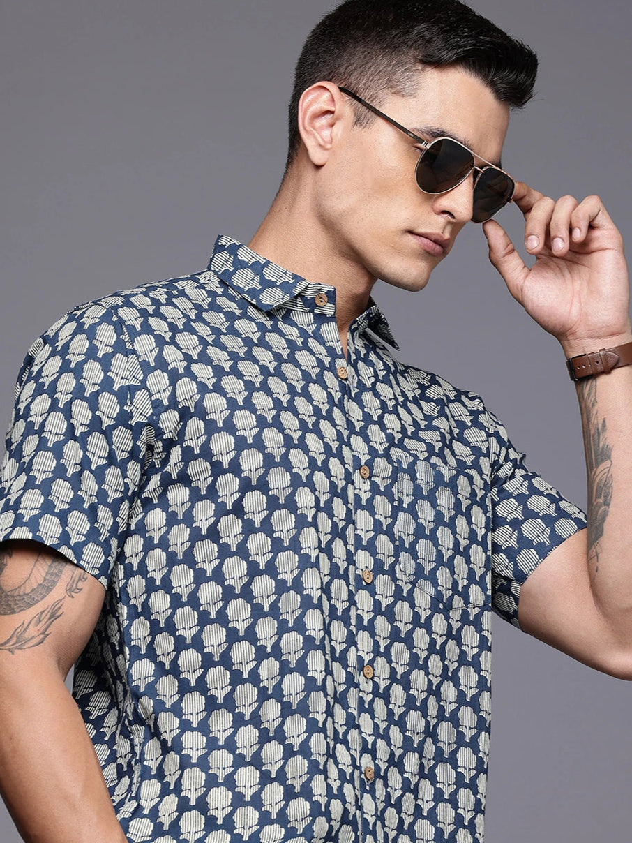 Man wearing a blue patterned shirt and sunglasses against a gray background