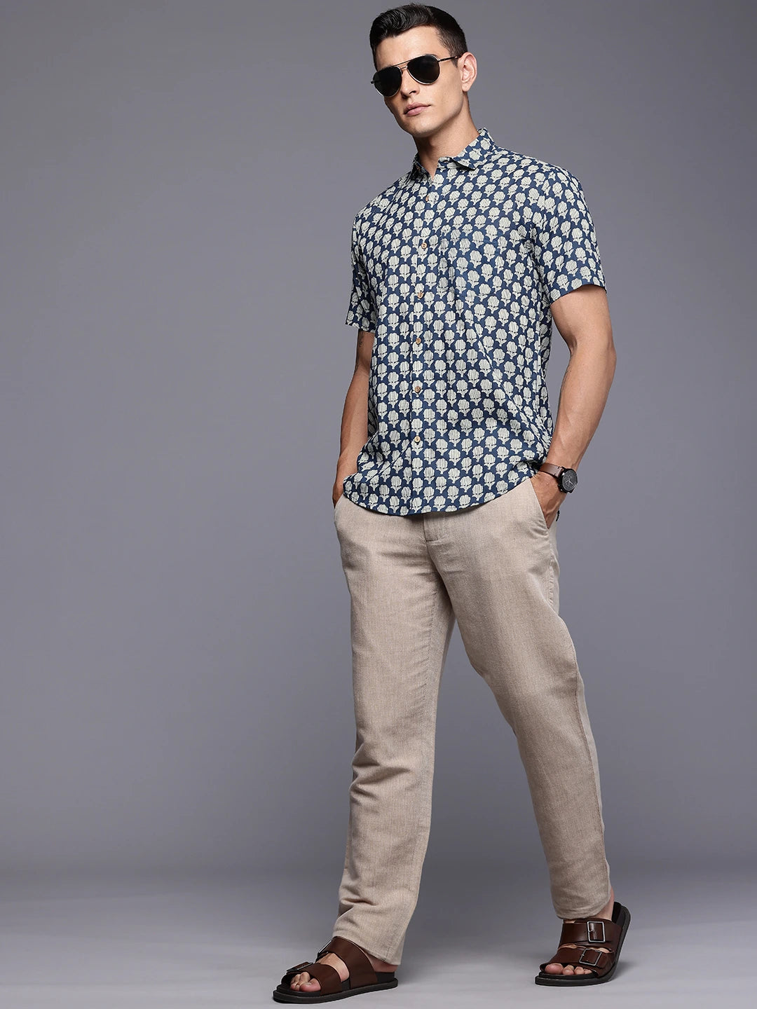 Man wearing a patterned shirt and beige pants against a gray background