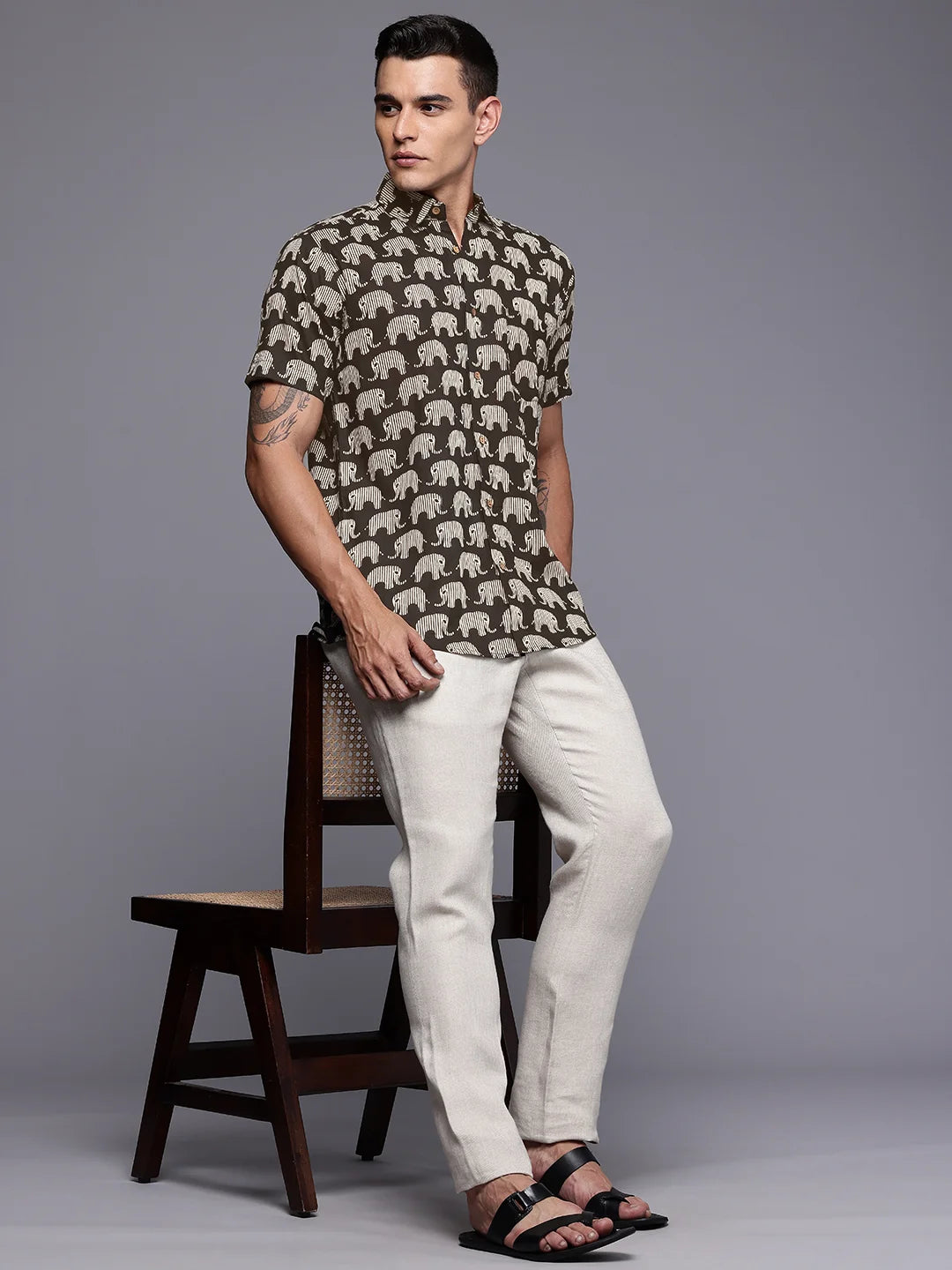 Man wearing a elephant printed shirt and sitting on a wooden stool