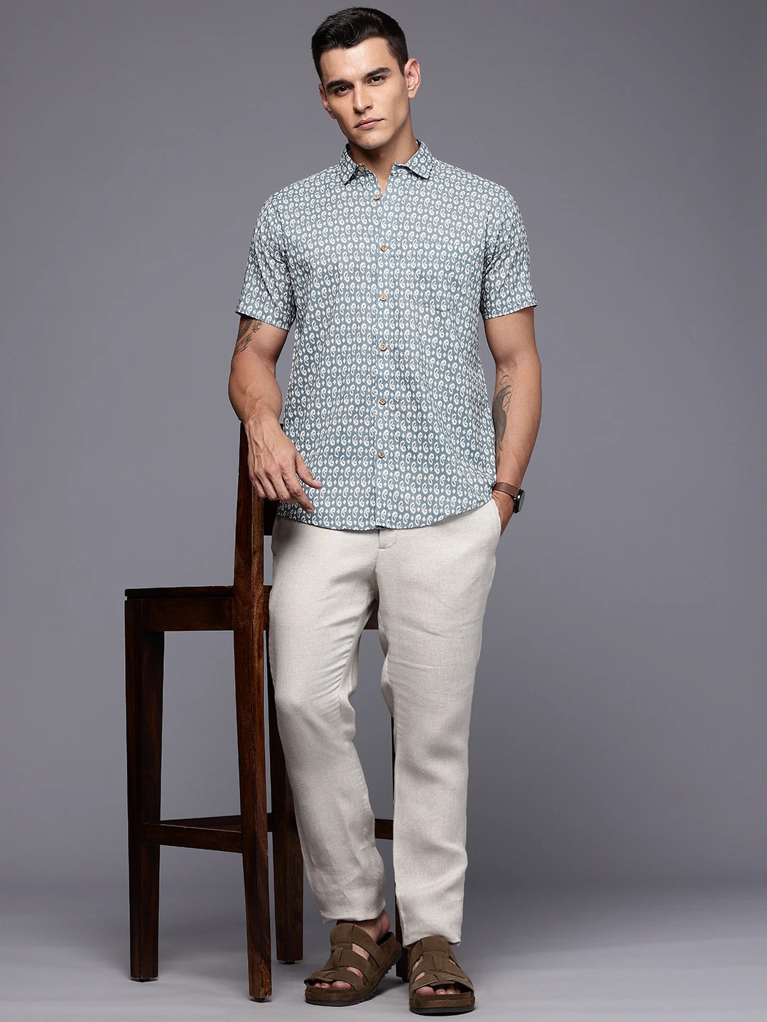 Man wearing a floral shirt standing next to a wooden chair