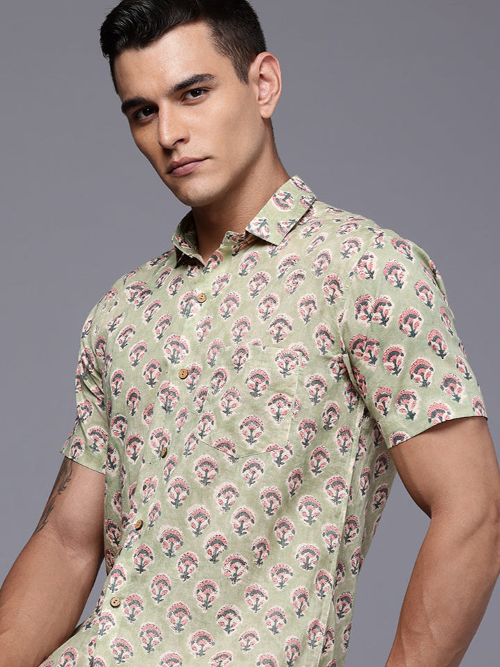Man wearing a green floral shirt sitting on a chair.