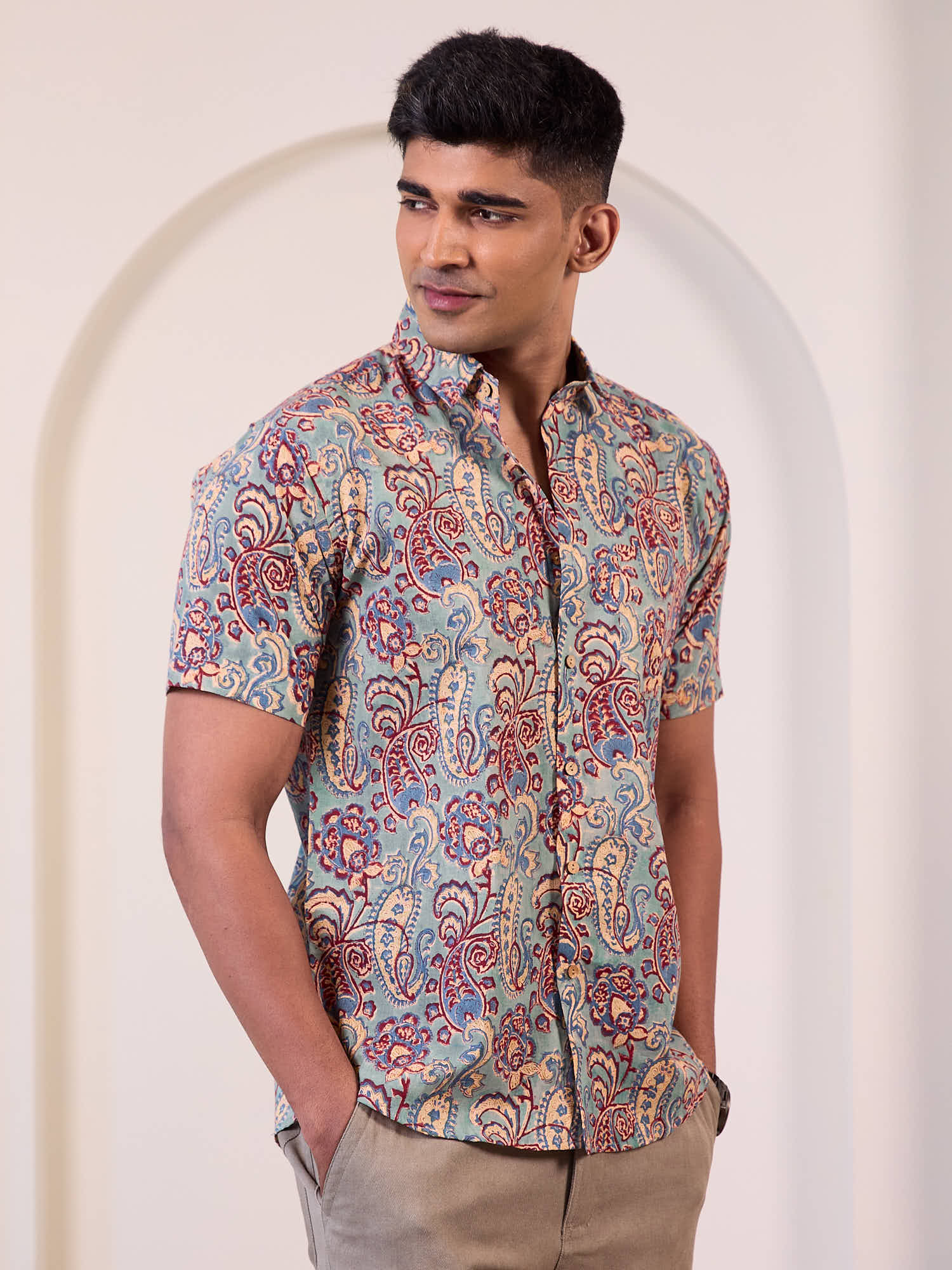 Man wearing a patterned shirt standing against a plain background