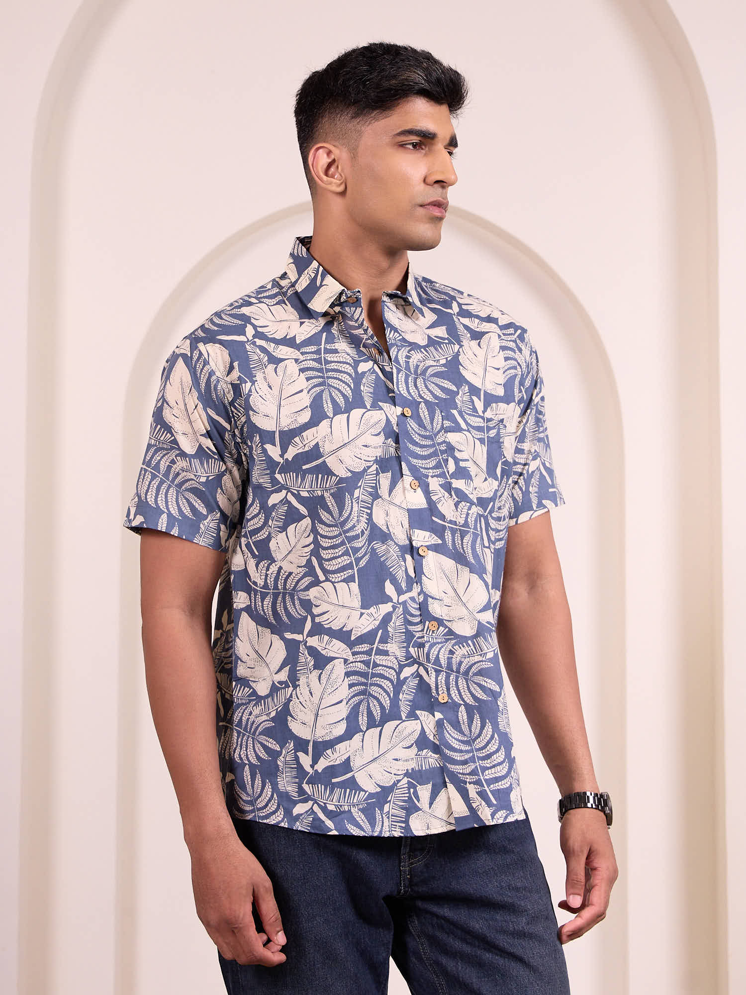 Man wearing a blue and grey leaf pattern shirt against a beige wall.