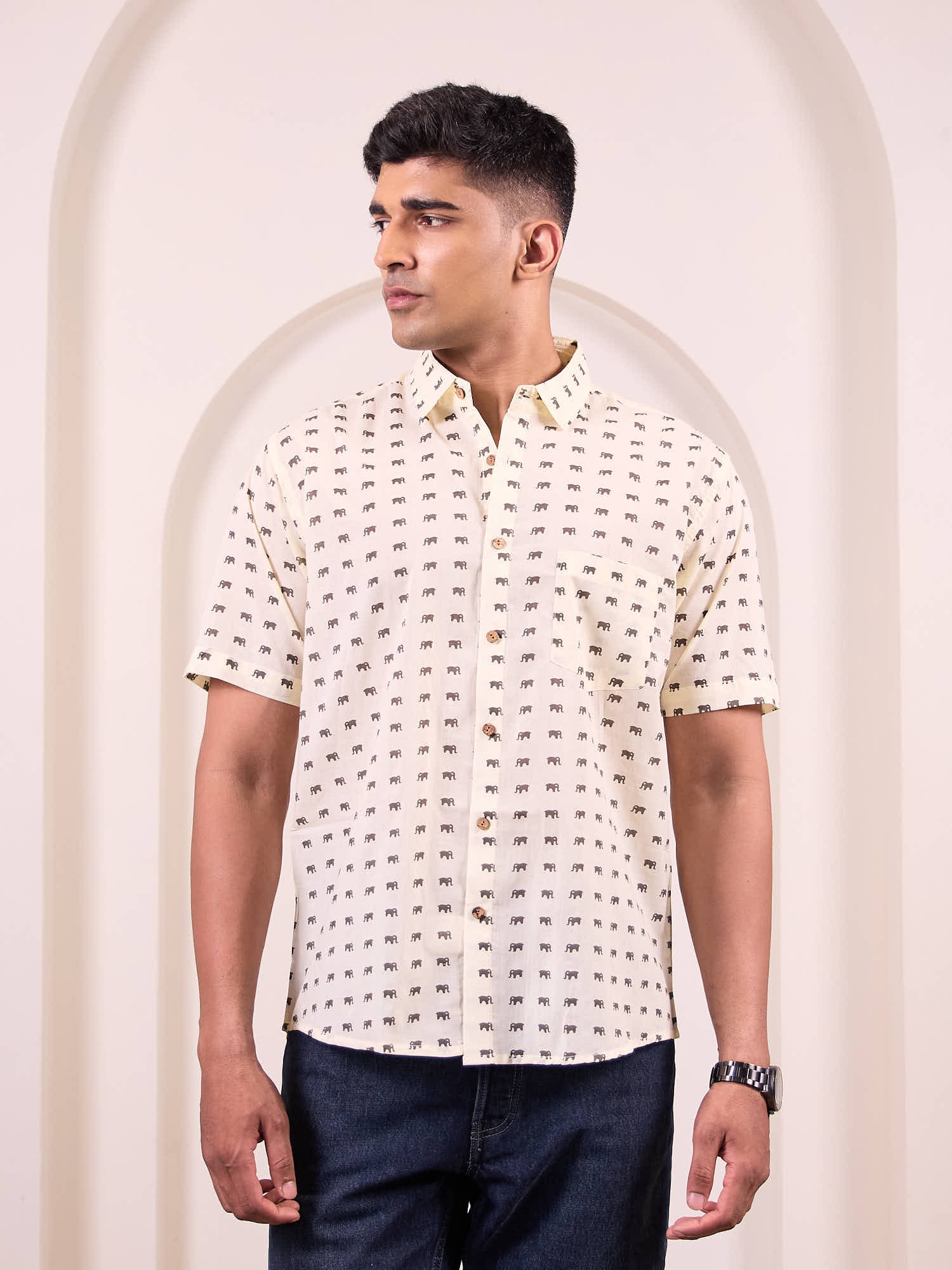 Man wearing a patterned white shirt standing in front of an archway.