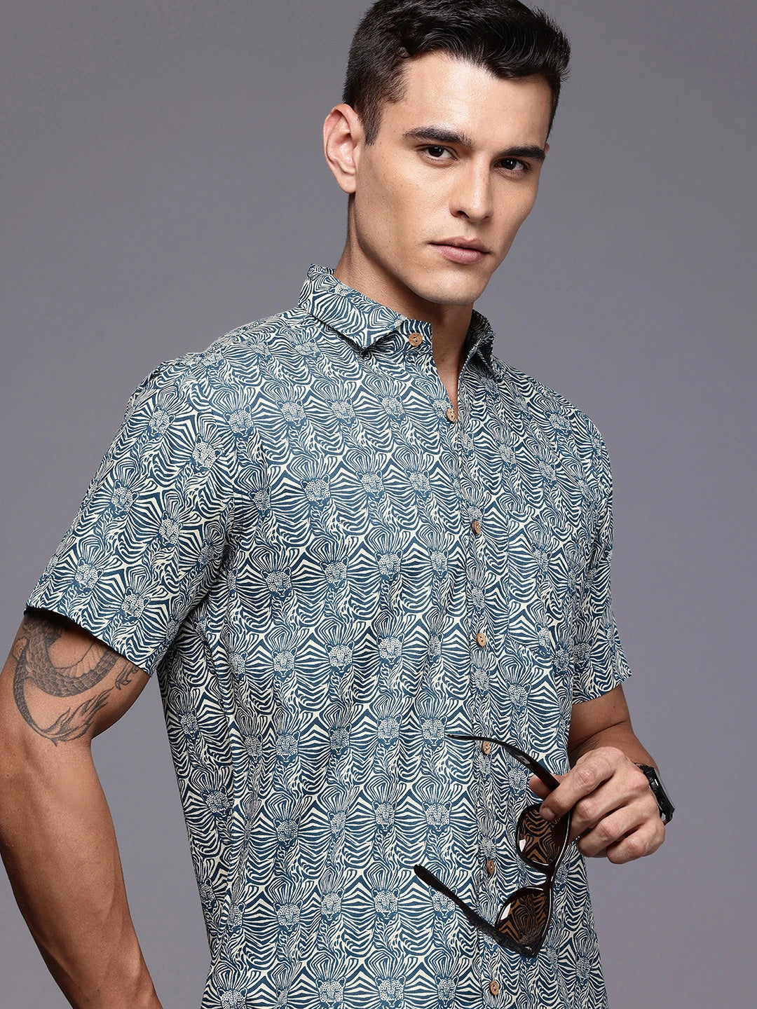 Man wearing a printed shirt holding sunglasses 